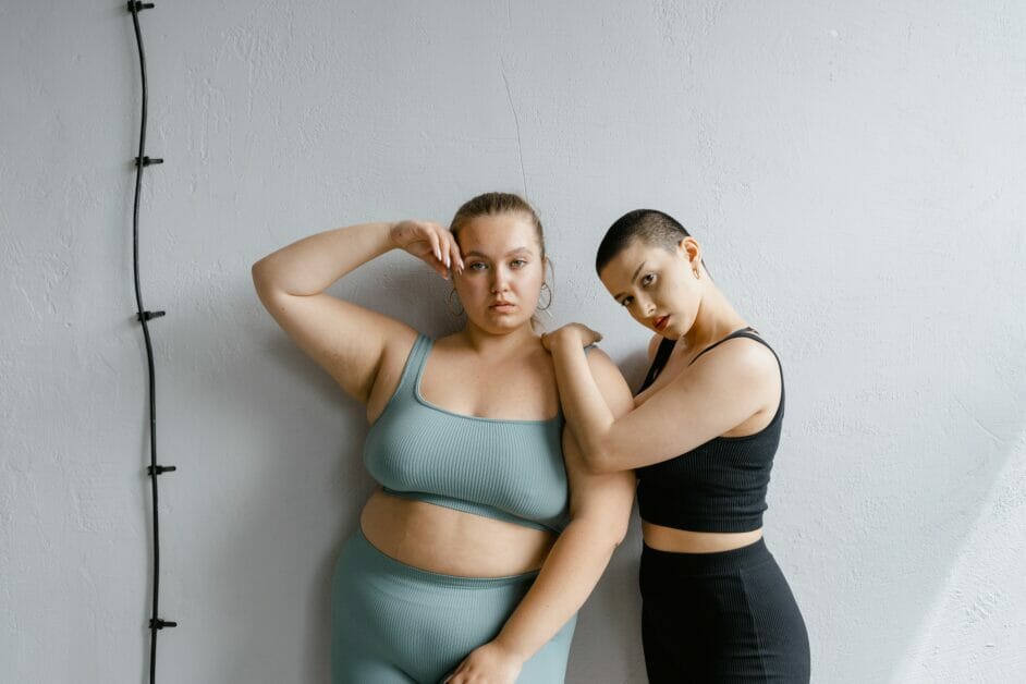 2 model women wearing gym wears posing in a white wall with a black wire rope backdrop