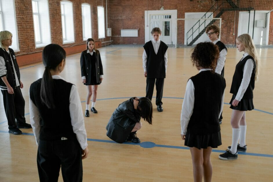 a girl student sitting at the center of a circled school girls and boys at the school gym