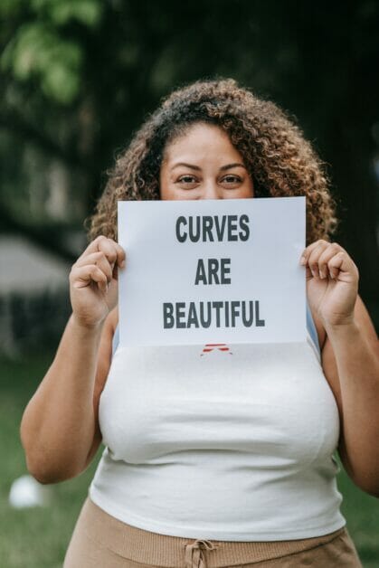 a plus size woman holding a bond paper with a message printed that says: CURVES ARE BEAUTIFUL