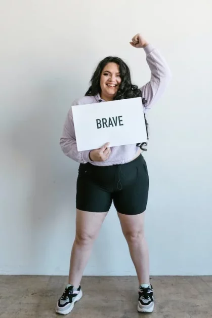 a plus size woman with a fist up and holding a "brave" placard