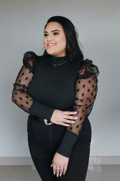 plus-size woman wearing a black blouse with a see-through long sleeve, black jeans accessorize with a belt