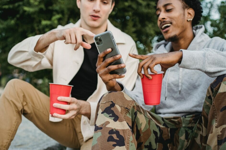 two men chilling outdoor looking at the phone while holding a red cup
