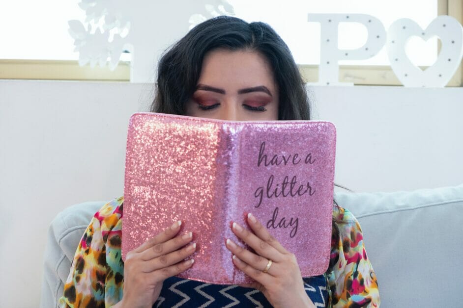 woman holding a pink glittery journal notebook with a quote printed that says: have a glitter day