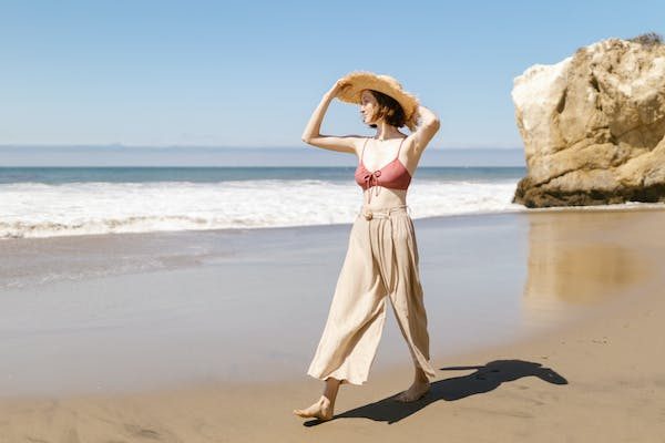 a woman with soft gamine kibbe body type walking at the beach with her summer hat