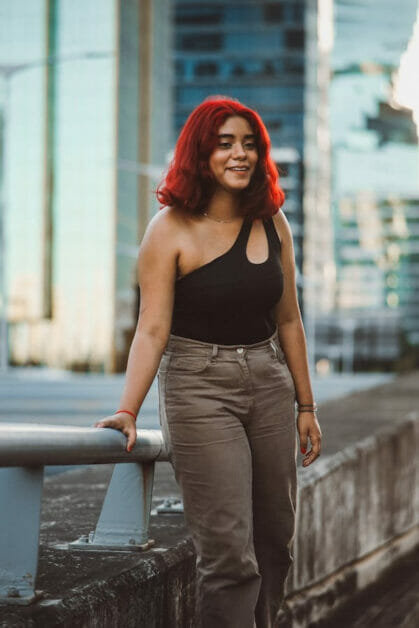 woman with red hair wearing black sleeveless top and a brown square high-waisted jeans