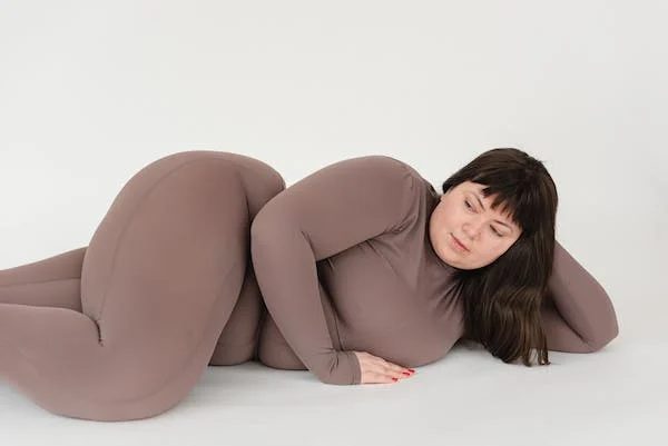 a plus size model wearing a brown yoga outfit laying on his side with left hand supporting her head