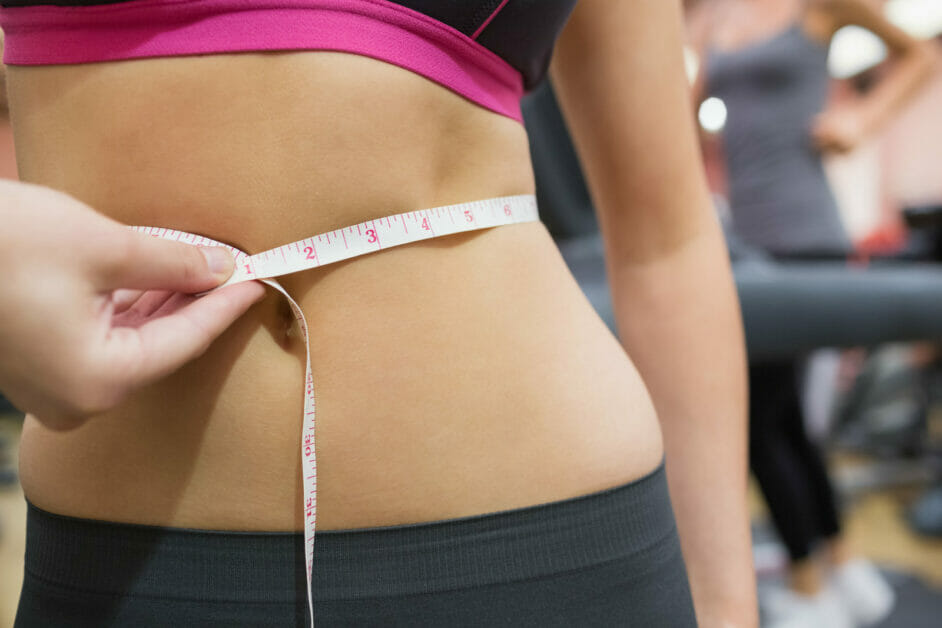 woman in the gym measuring her waistline with a measuring tape